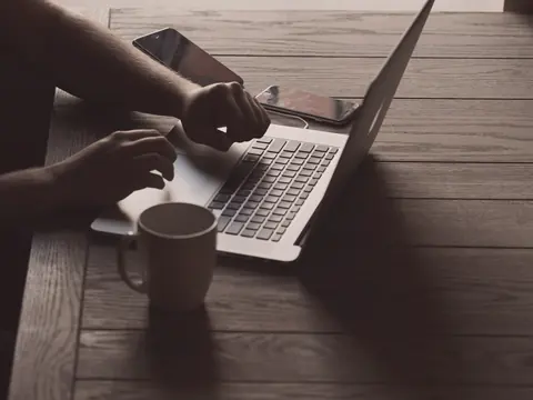 Eine Person arbeitet allein am Laptop an einem Holztisch, daneben eine Tasse